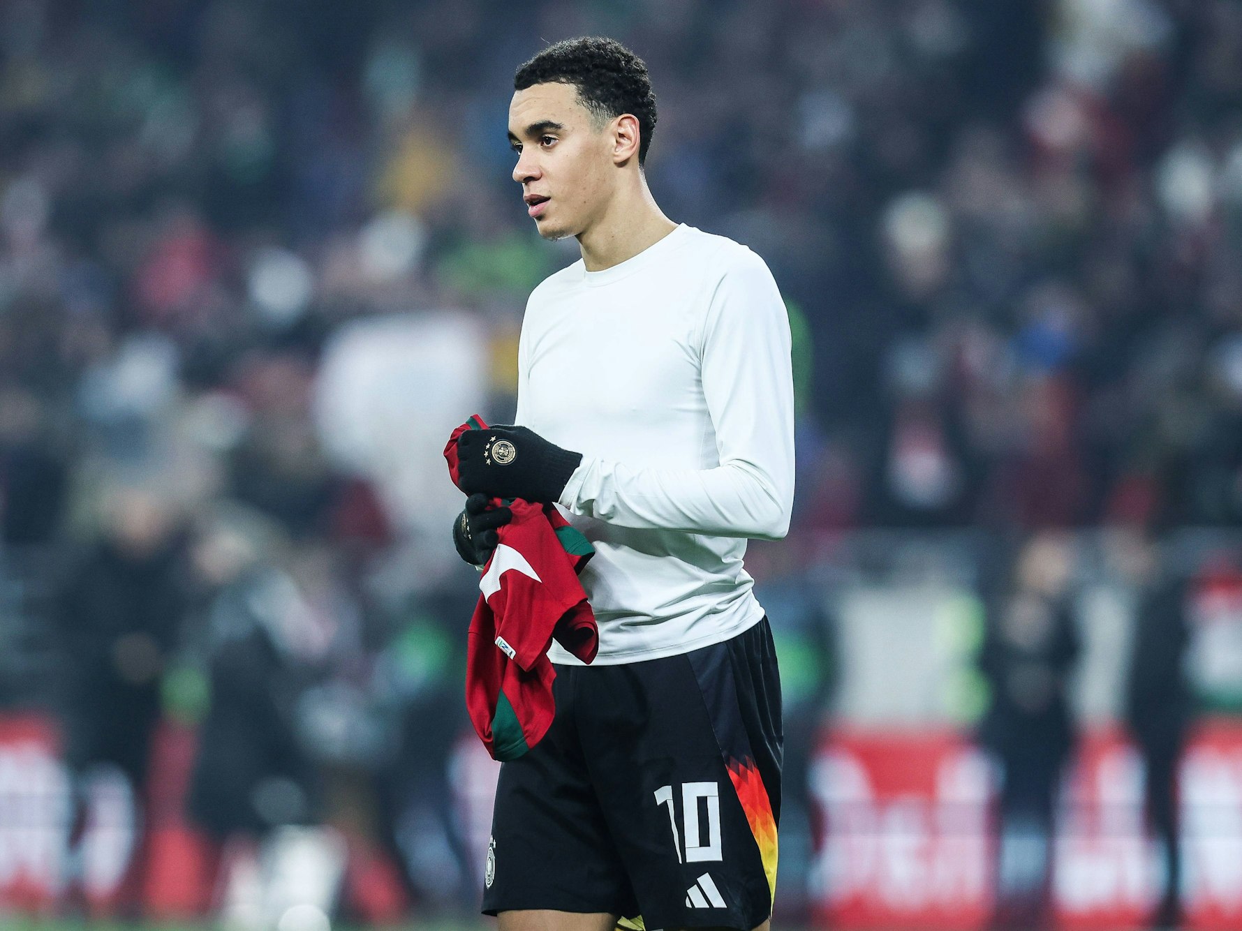 Jamal Musiala hält nach dem Trikottausch ein Shirt in den Händen.