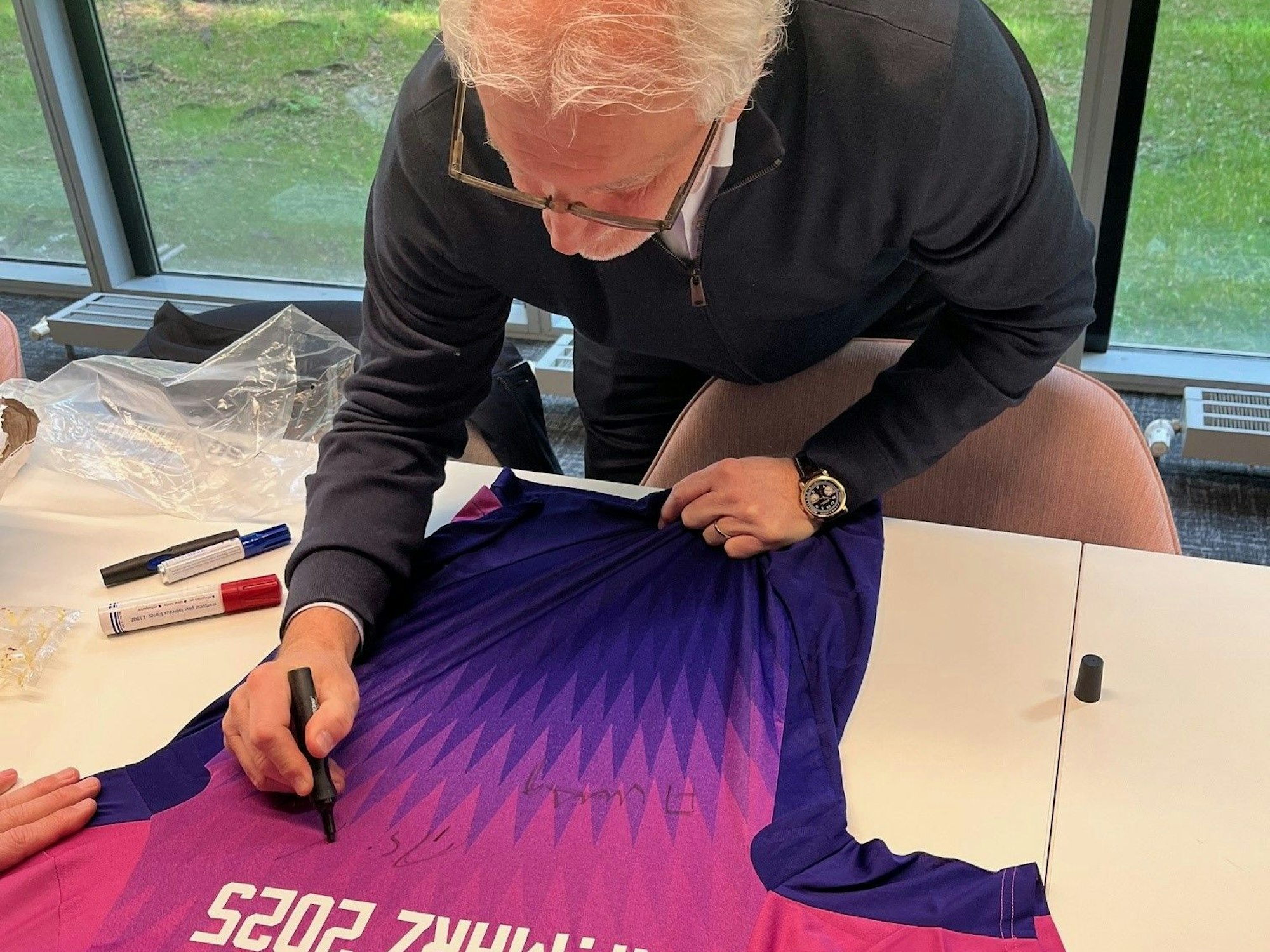 Rudi Völler unterschreibt auf einem Trikot.