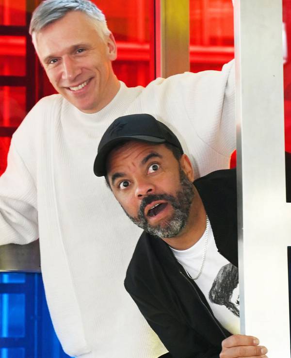 Bastian Campmann und Simon Pearce albern in einer Telefonzelle herum.