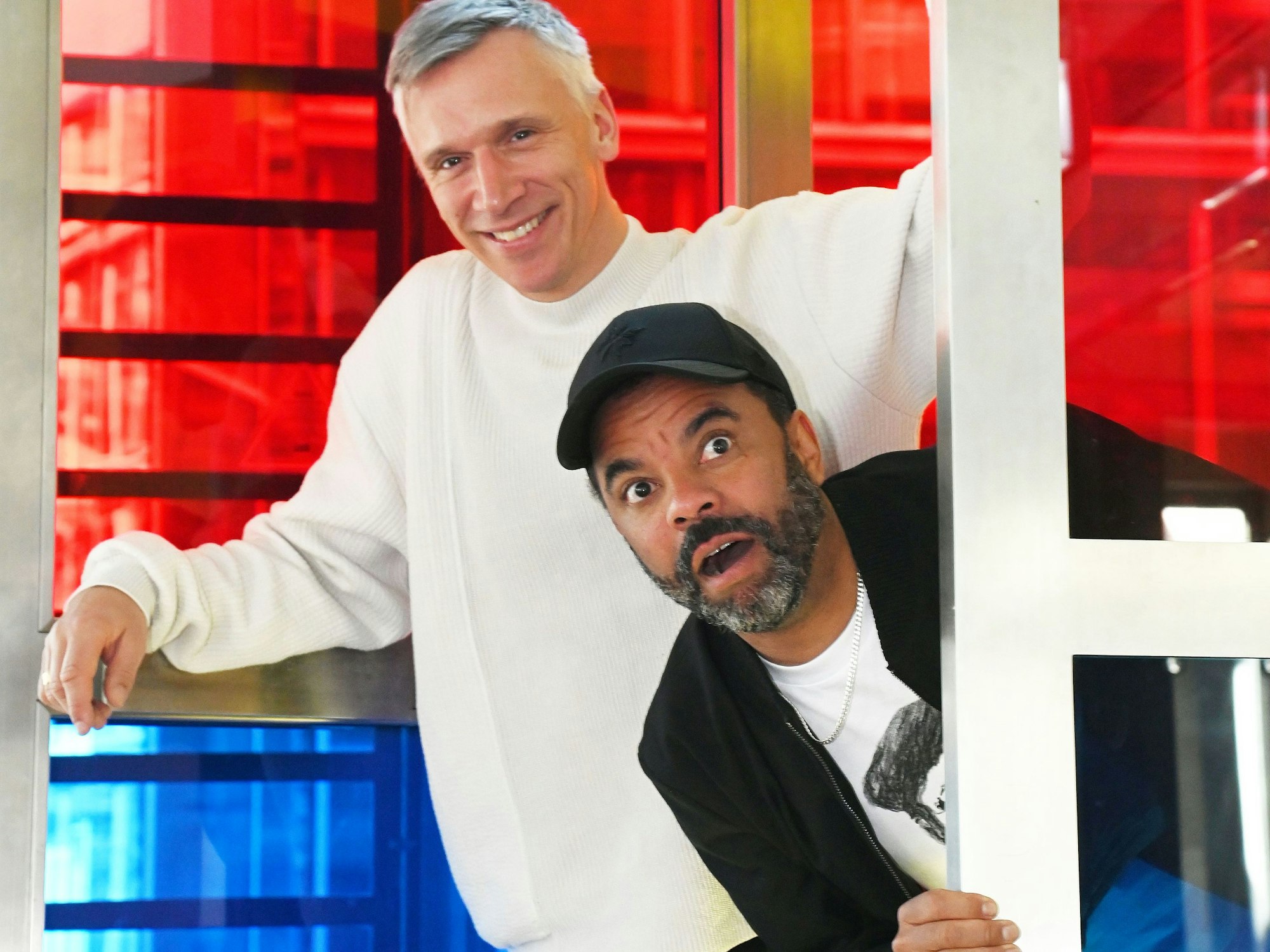 Bastian Campmann und Simon Pearce albern in einer Telefonzelle herum.