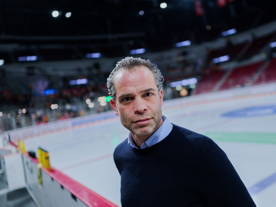 Niki Mondt steht vor der Eisfläche an der Bande und guckt in die Kamera.