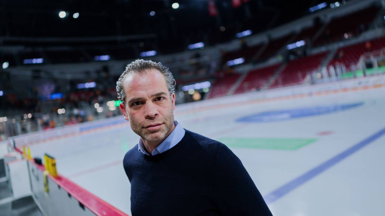 Niki Mondt steht vor der Eisfläche an der Bande und guckt in die Kamera.