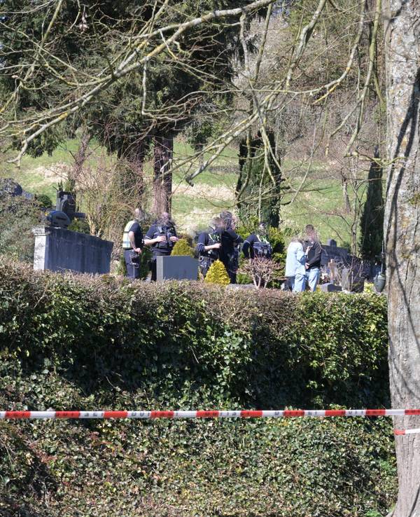 Ein Friedhof ist mit Polizei-Flatterband abgesperrt, zwischen Gräbern stehen unter anderem Polizeikräfte.