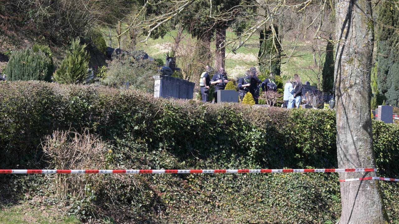 Ein Friedhof ist mit Polizei-Flatterband abgesperrt, zwischen Gräbern stehen unter anderem Polizeikräfte.