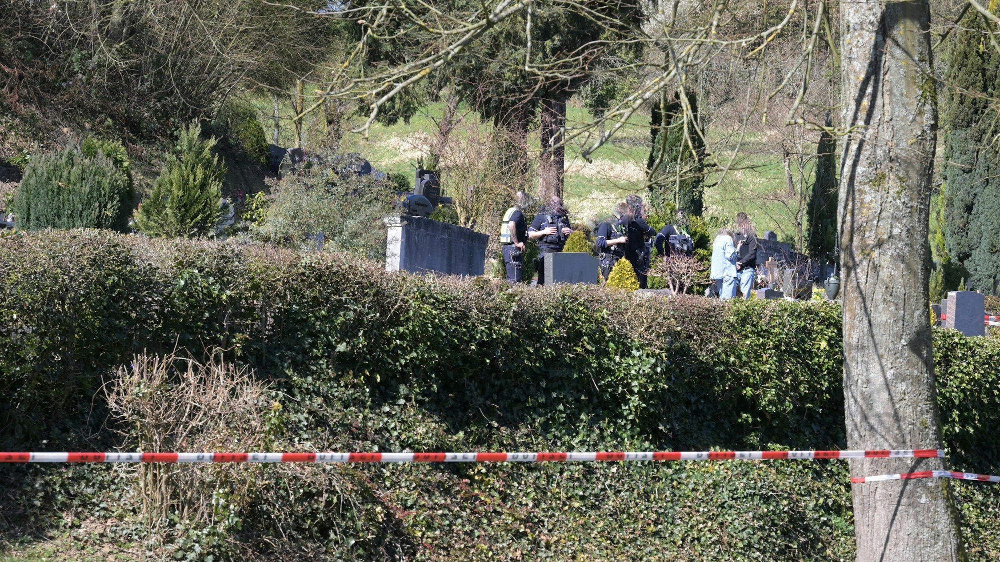 Die Polizei hat einen Friedhof abgesperrt, zwischen den Gräbern sind Polizeikräfte im Einsatz.