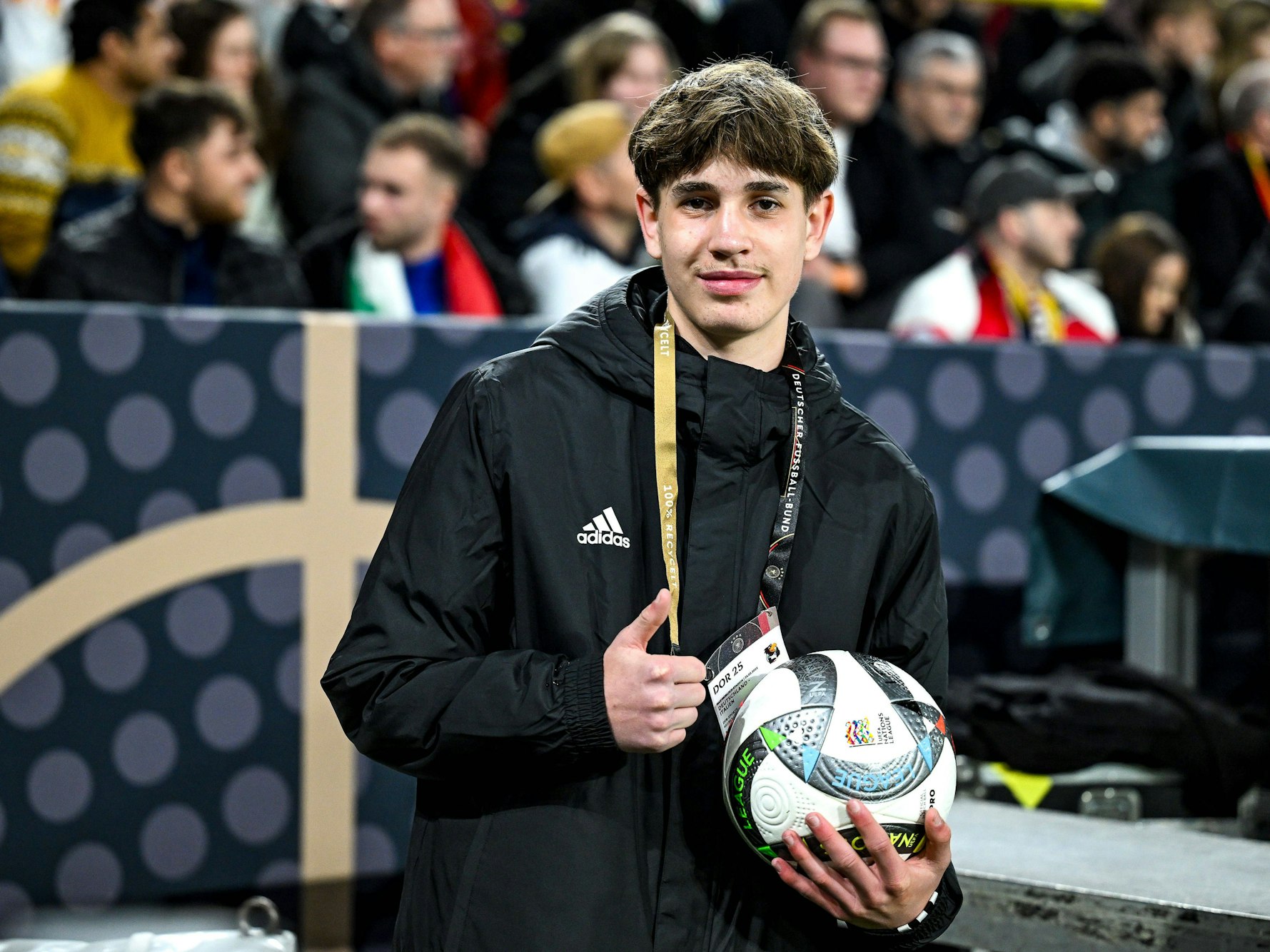 Der Balljunge, der Joshua Kimmich den Ball vor dem Eckball schnell zugeworfen hatte, lächelt in die Kamera und zeigt mit dem Daumen nach oben.