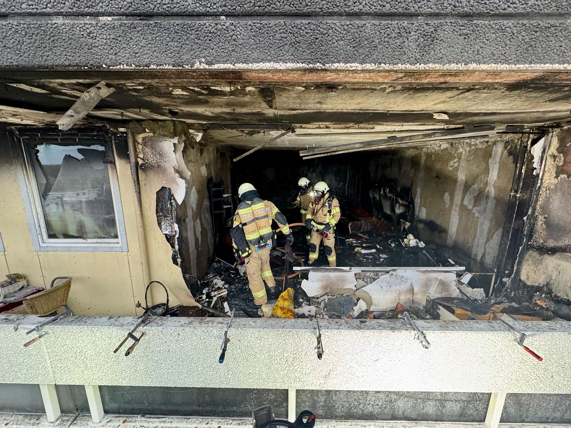 Drei Feuerwehrleute stehen in einer völlig ausgebrannten Wohnung.