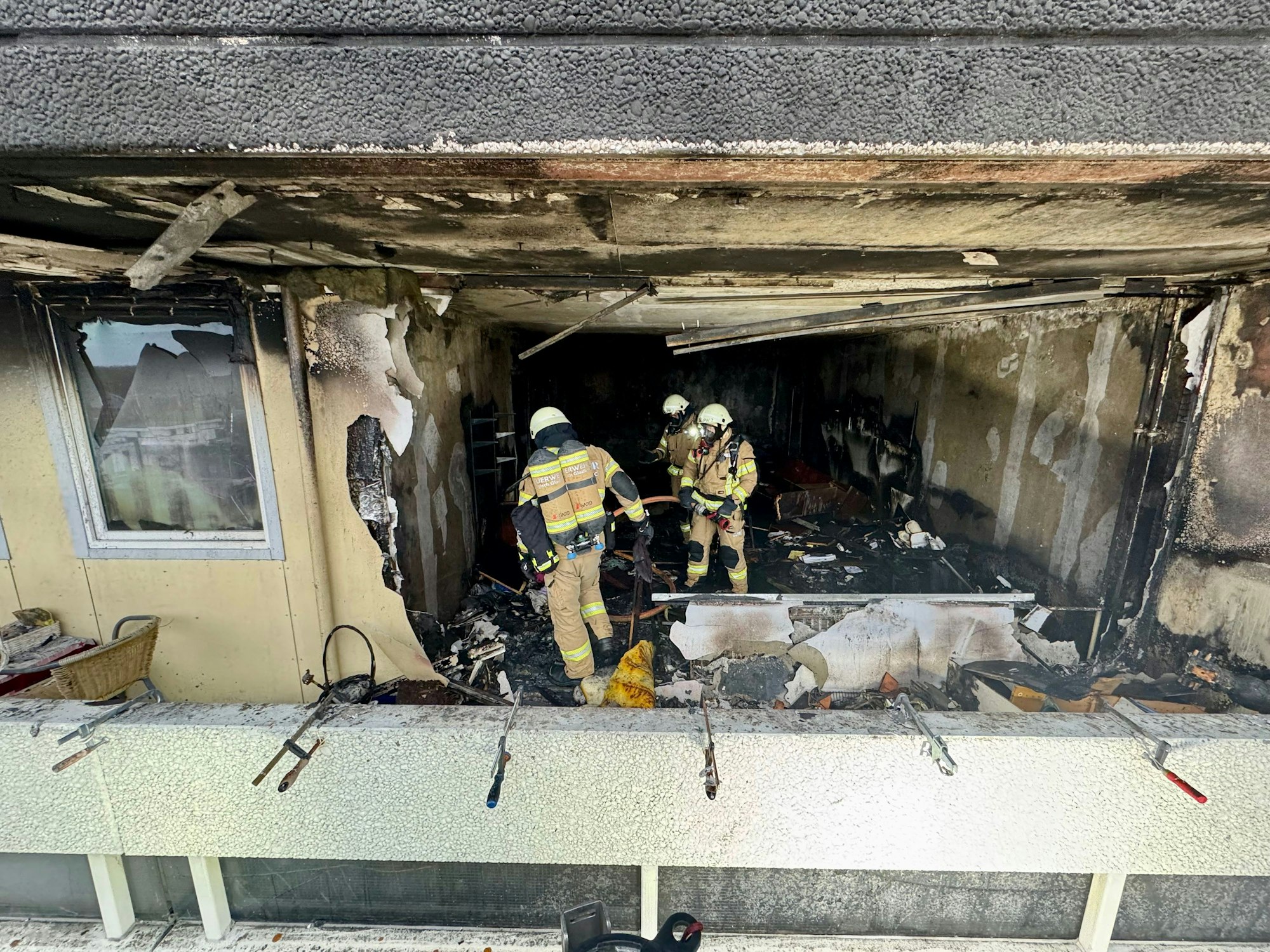 Drei Feuerwehrleute stehen in einer völlig ausgebrannten Wohnung.