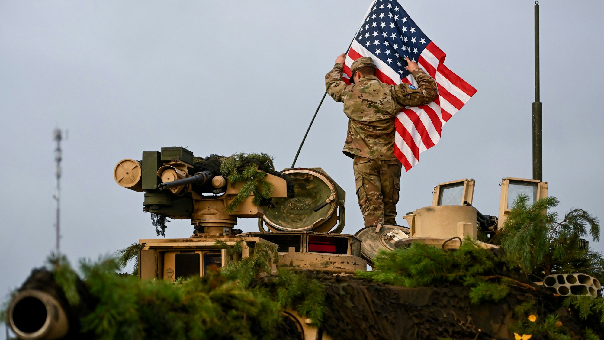 Ein Soldat bringt während einer Militärübung in Litauen auf dem Truppenübungsplatz Pabrade eine US-amerikanische Fahne an einem Militärfahrzeug an (Archivbild).