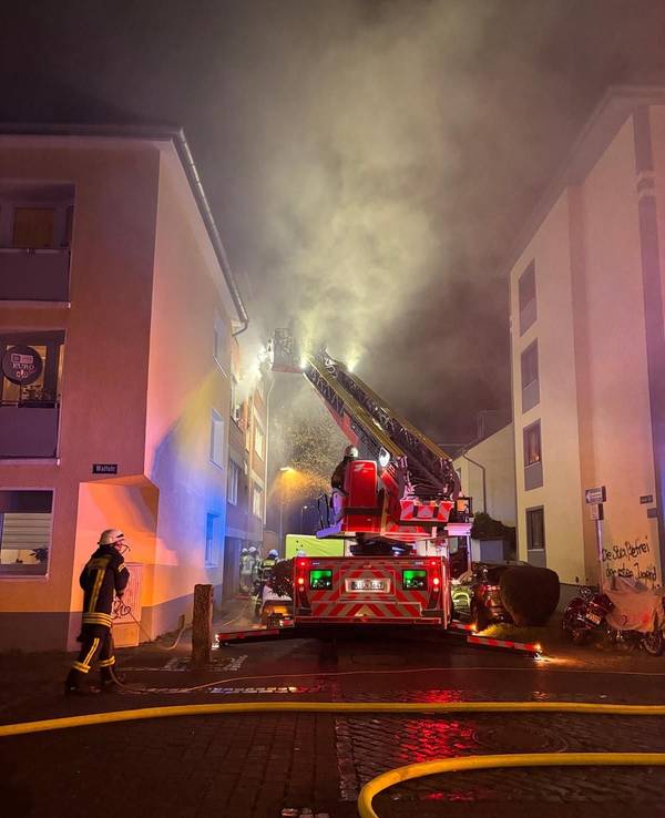Aus einem Fenster im zweiten Stock dringt starker Rauch, vor dem Haus steht ein Fahrzeug der Feuerwehr, sind mehrere Wehrleute im Einsatz.