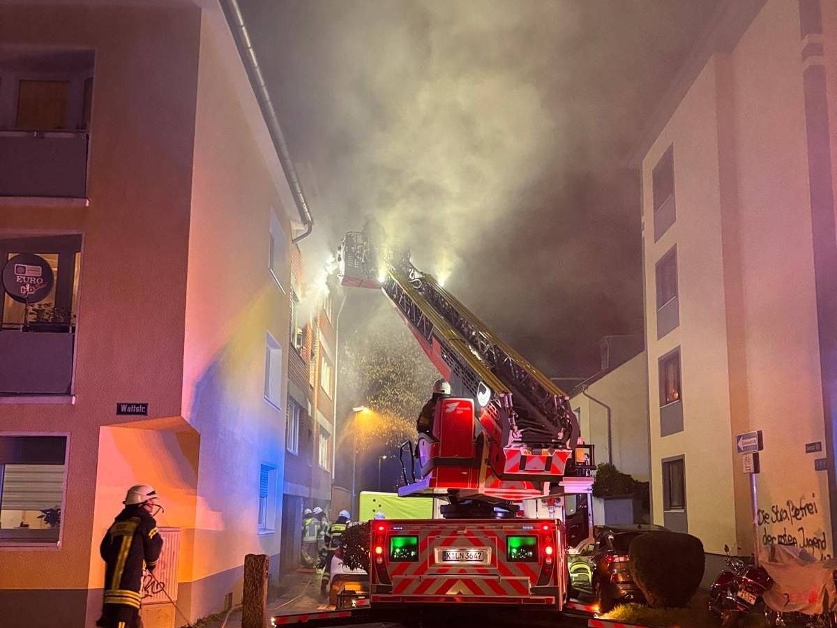 Aus einem Fenster im zweiten Stock dringt starker Rauch, vor dem Haus steht ein Fahrzeug der Feuerwehr, sind mehrere Wehrleute im Einsatz.