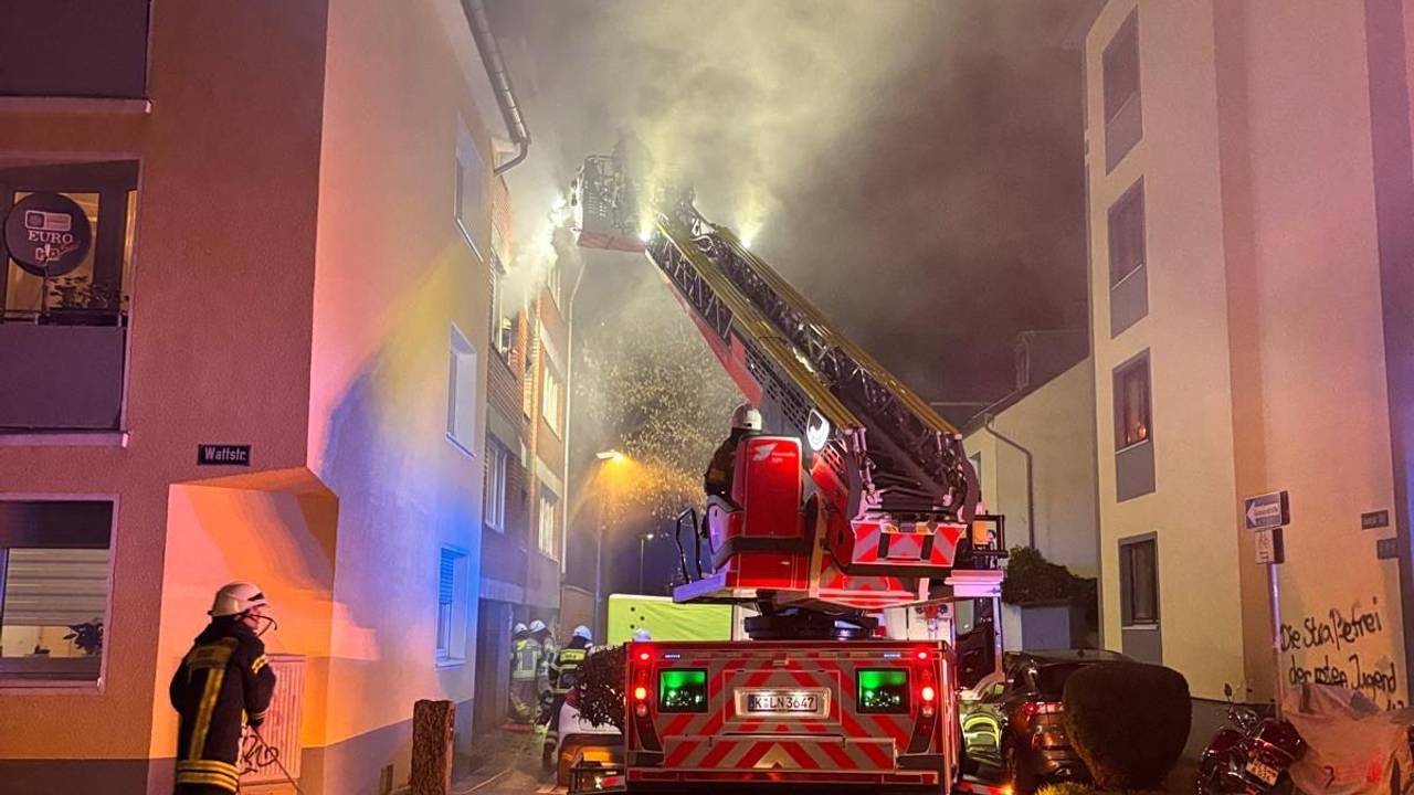 Aus einem Fenster im zweiten Stock dringt starker Rauch, vor dem Haus steht ein Fahrzeug der Feuerwehr, sind mehrere Wehrleute im Einsatz.