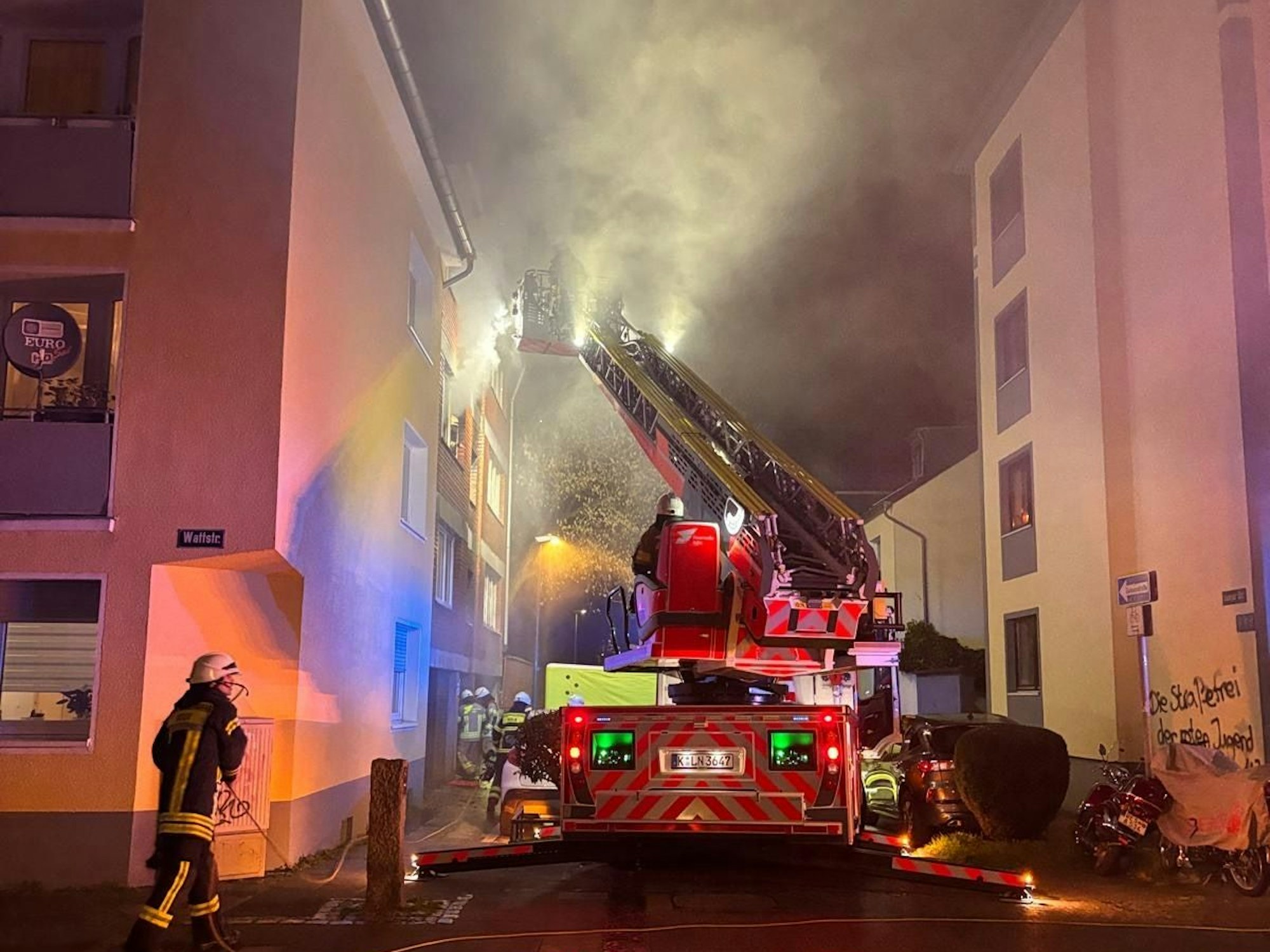 Aus einem Hausfenster dringt Qualm, die Feuerwehr löscht über die Drehleiter.