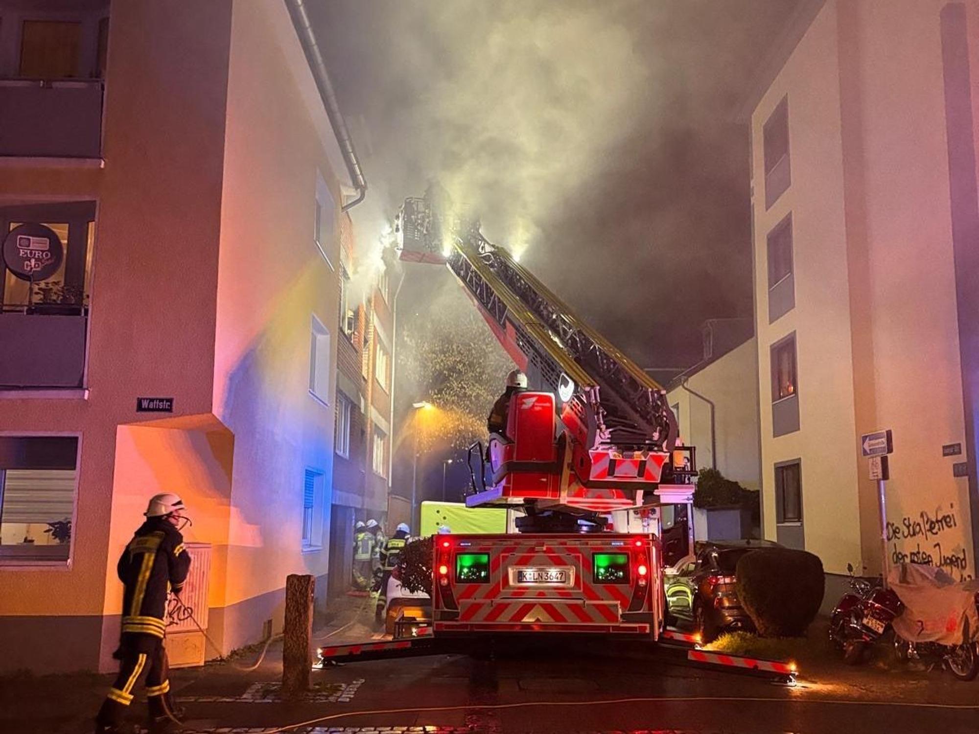 Aus einem Fenster im zweiten Stock dringt starker Rauch, vor dem Haus steht ein Fahrzeug der Feuerwehr, sind mehrere Wehrleute im Einsatz.