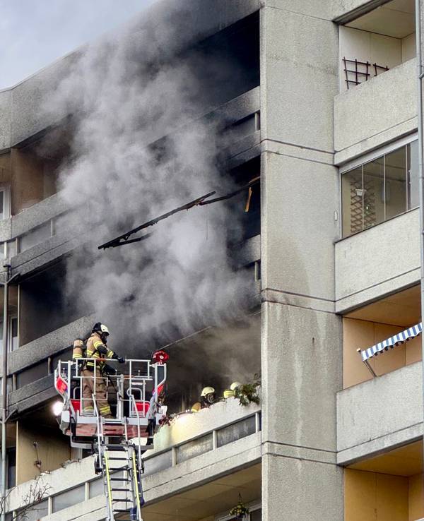 Aus einem Balkon steigt dichter Rauch, davor ein Feuerwehrmann auf einer Drehleiter.
