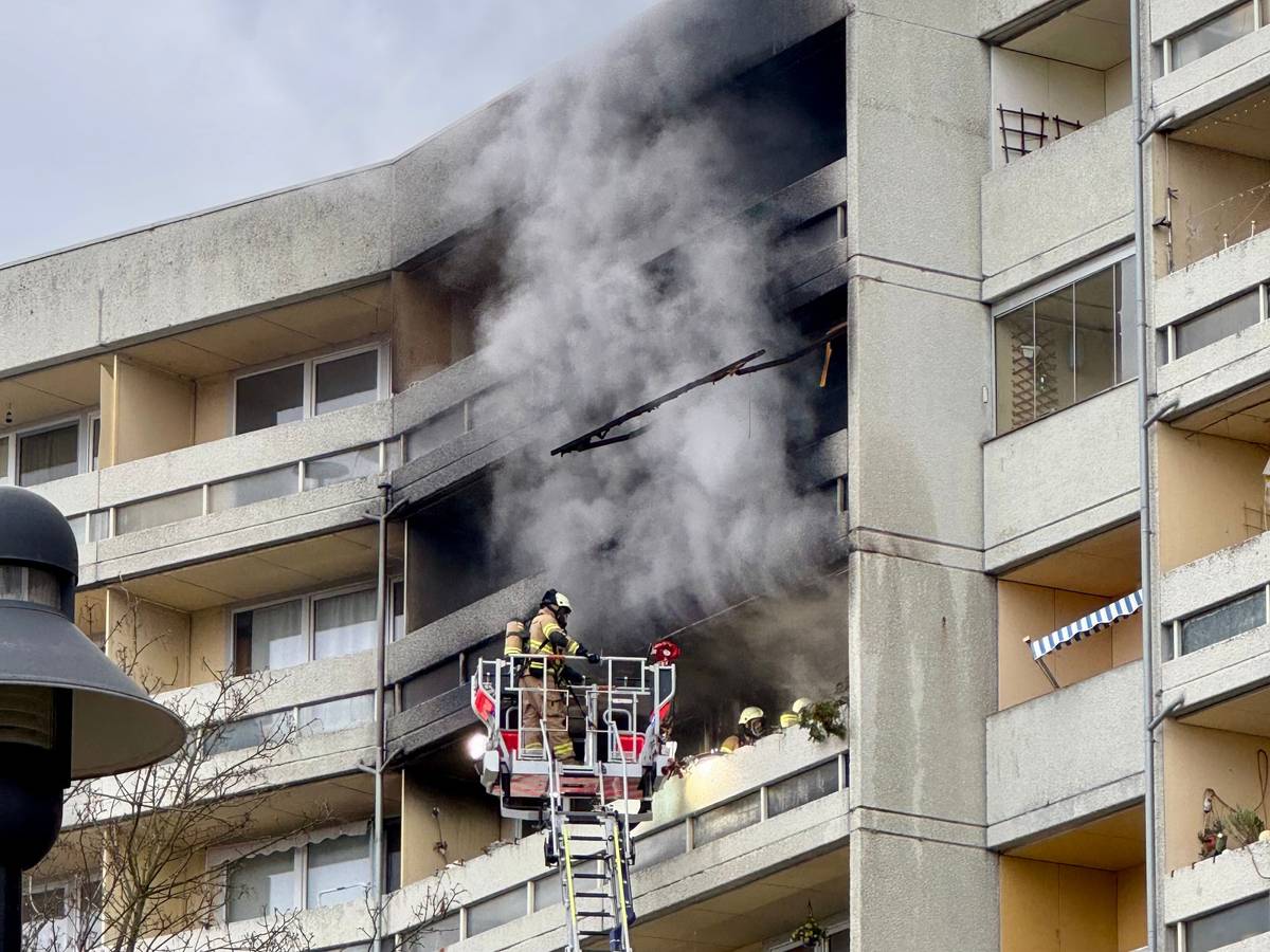 Aus einem Balkon steigt dichter Rauch, davor ein Feuerwehrmann auf einer Drehleiter.
