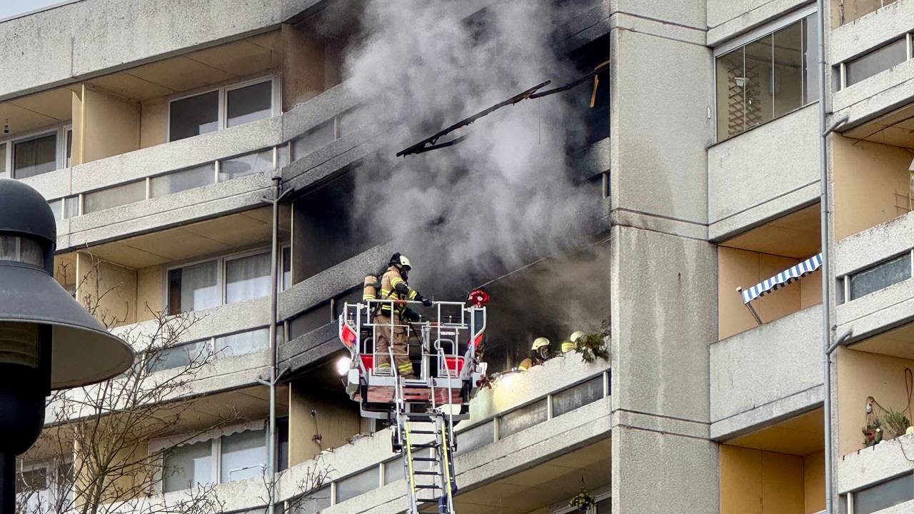 Aus einem Balkon steigt dichter Rauch, davor ein Feuerwehrmann auf einer Drehleiter.