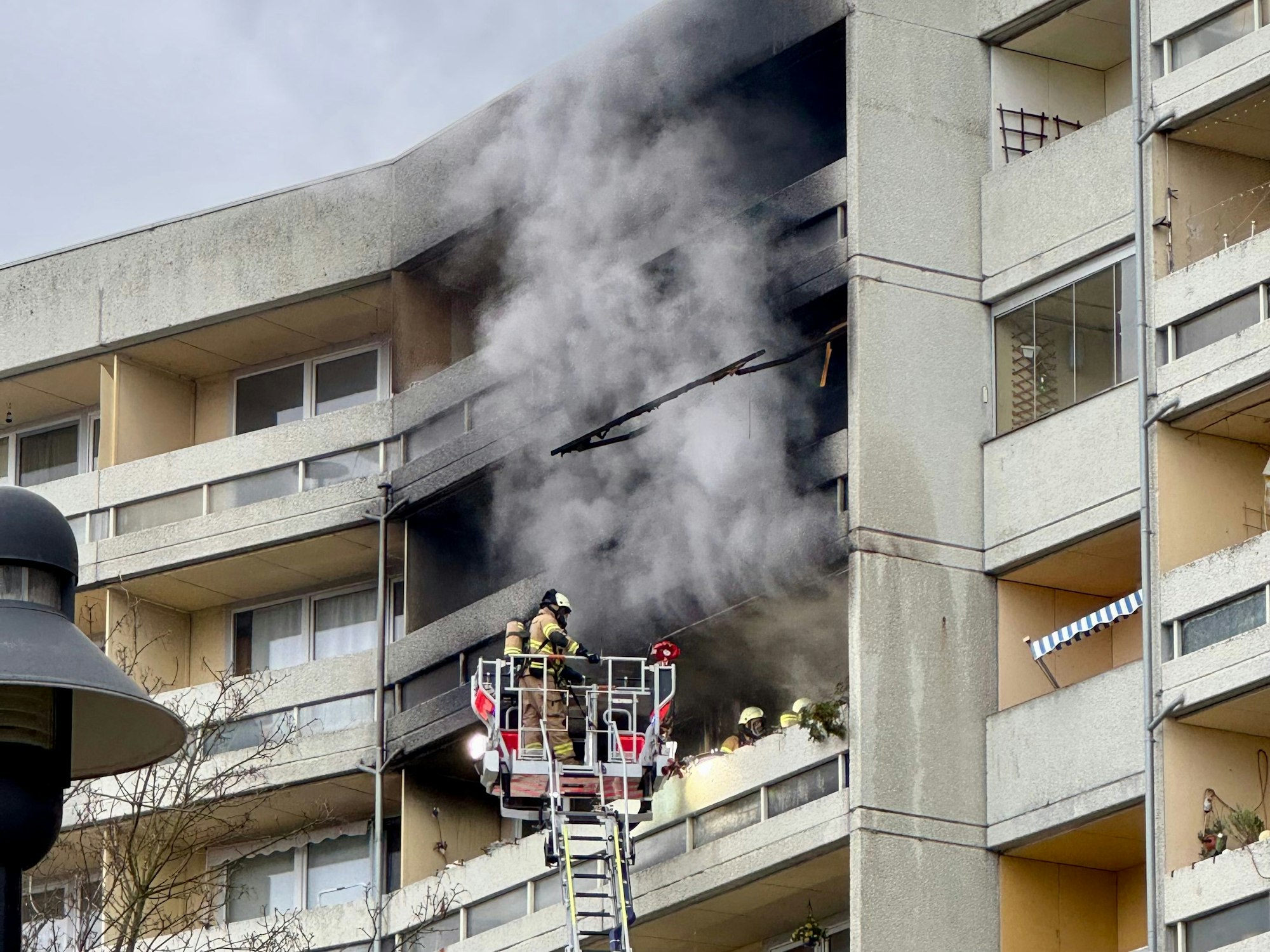 Aus einem Balkon steigt dichter Rauch, davor ein Feuerwehrmann auf einer Drehleiter.