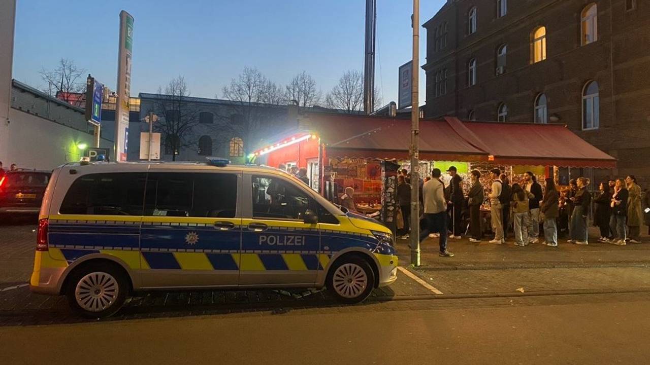 Ein Polizeifahrzeug hält vor einem Imbiss, vor dem die Leute Schlange stehen.