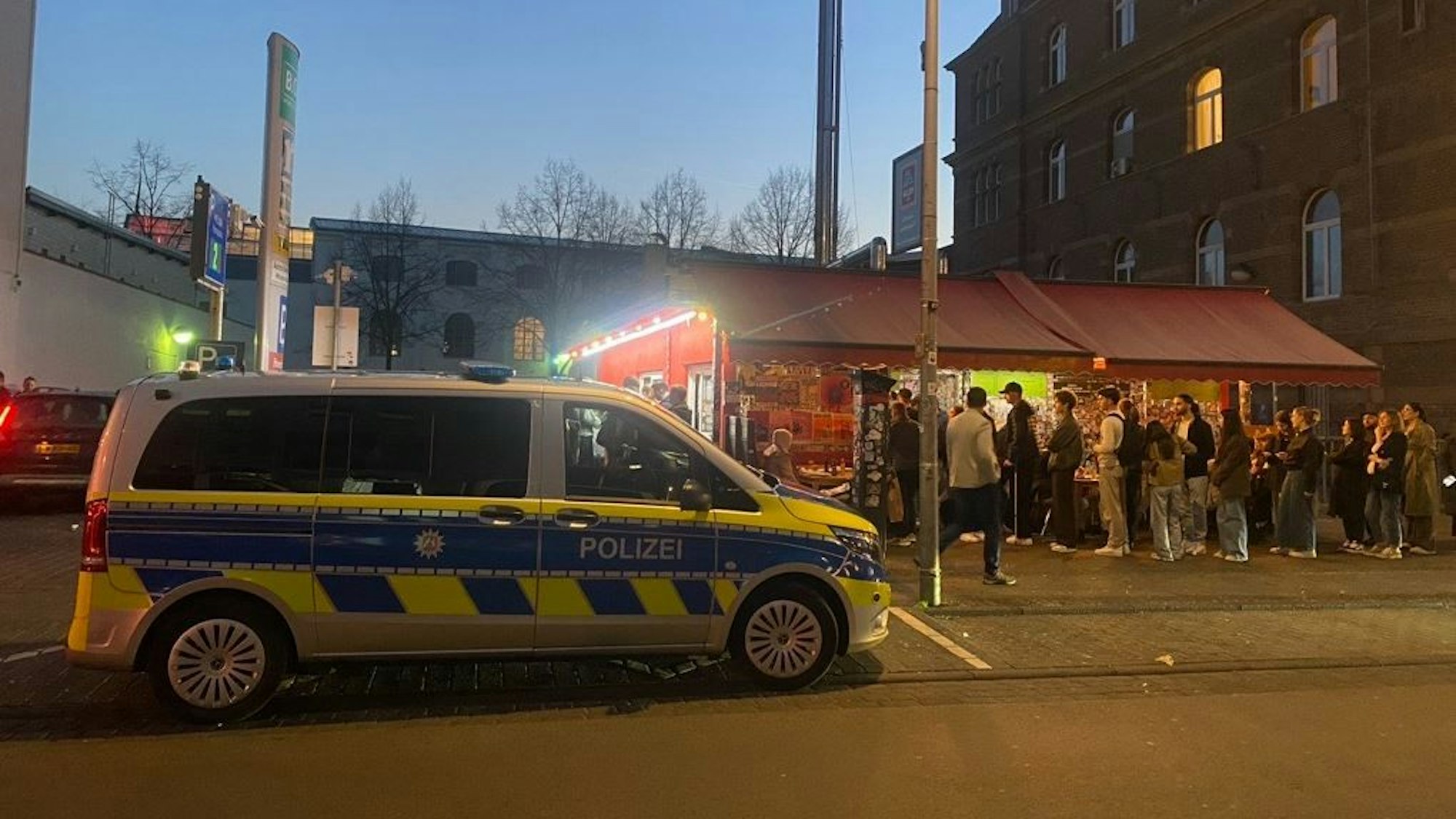 Ein Polizeifahrzeug hält vor einem Imbiss, vor dem die Leute Schlange stehen.