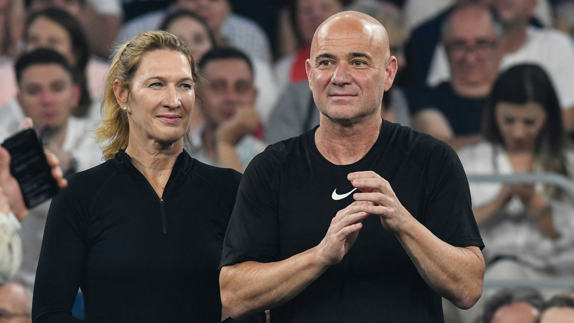 Steffi Graf steht neben Andre Agassi auf einem Tennisplatz.