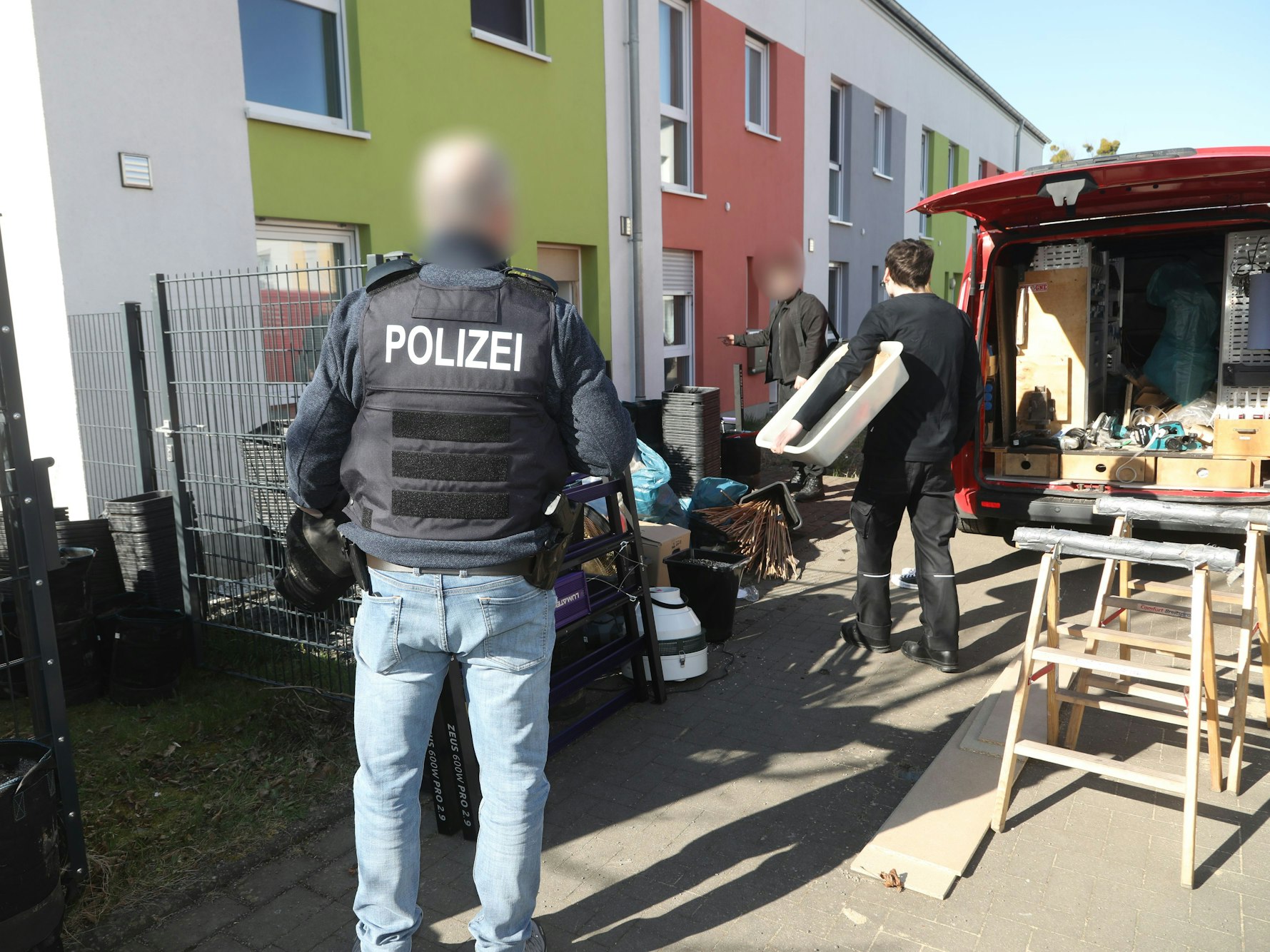 Ein Polizist steht vor einer Häuserreihe, während zwei Kollegen in die Richtung eines der Häuser gehen.