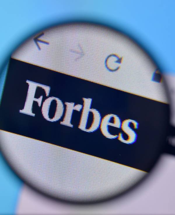 Zu sehen ist eine Lupe die das Logo der „Forbes“-Onlineseite vergrößert.