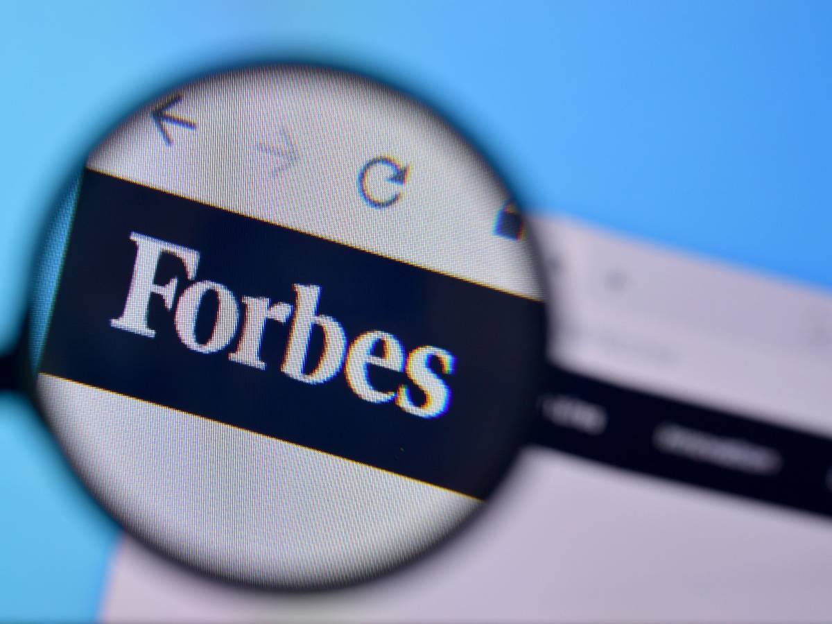 Zu sehen ist eine Lupe die das Logo der „Forbes“-Onlineseite vergrößert.