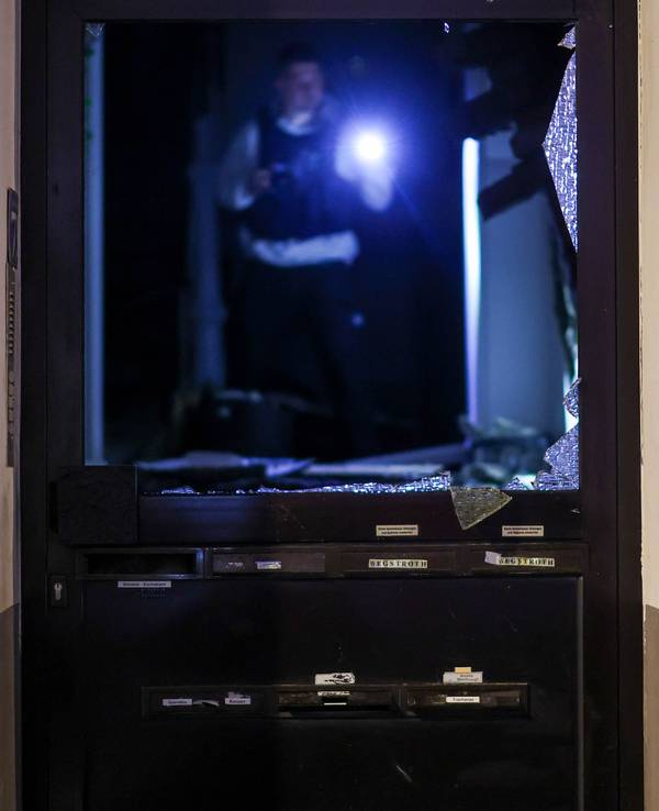Ein Polizeibeamter der Spurensicherung untersucht im Hausflur den Tatort, durch die Explosion im Erdgeschoss des Hauses wurde die Hauseingangstüre beschädigt.