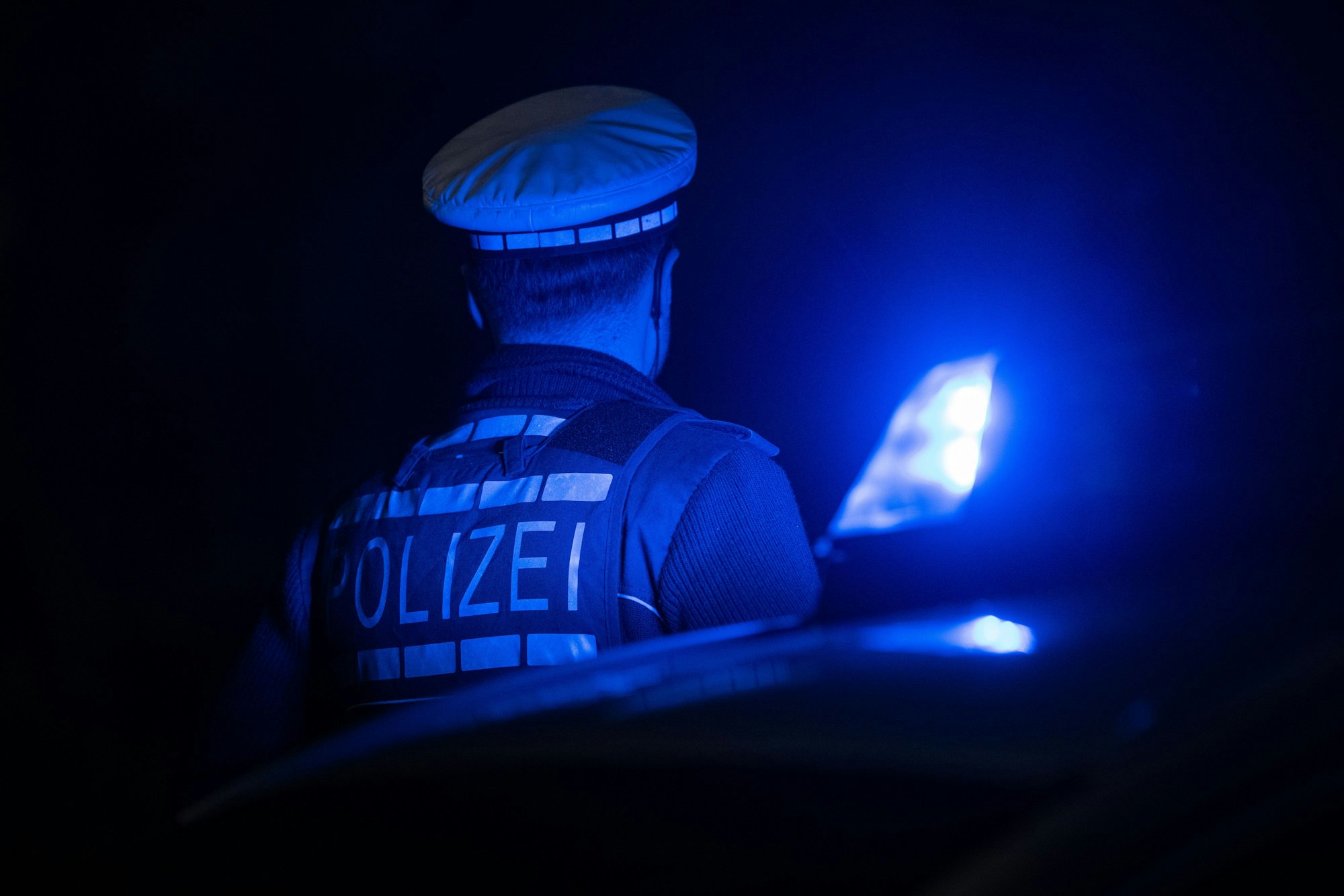 Ein Polizist im Schein des Blaulichts eines Polizeiautos.