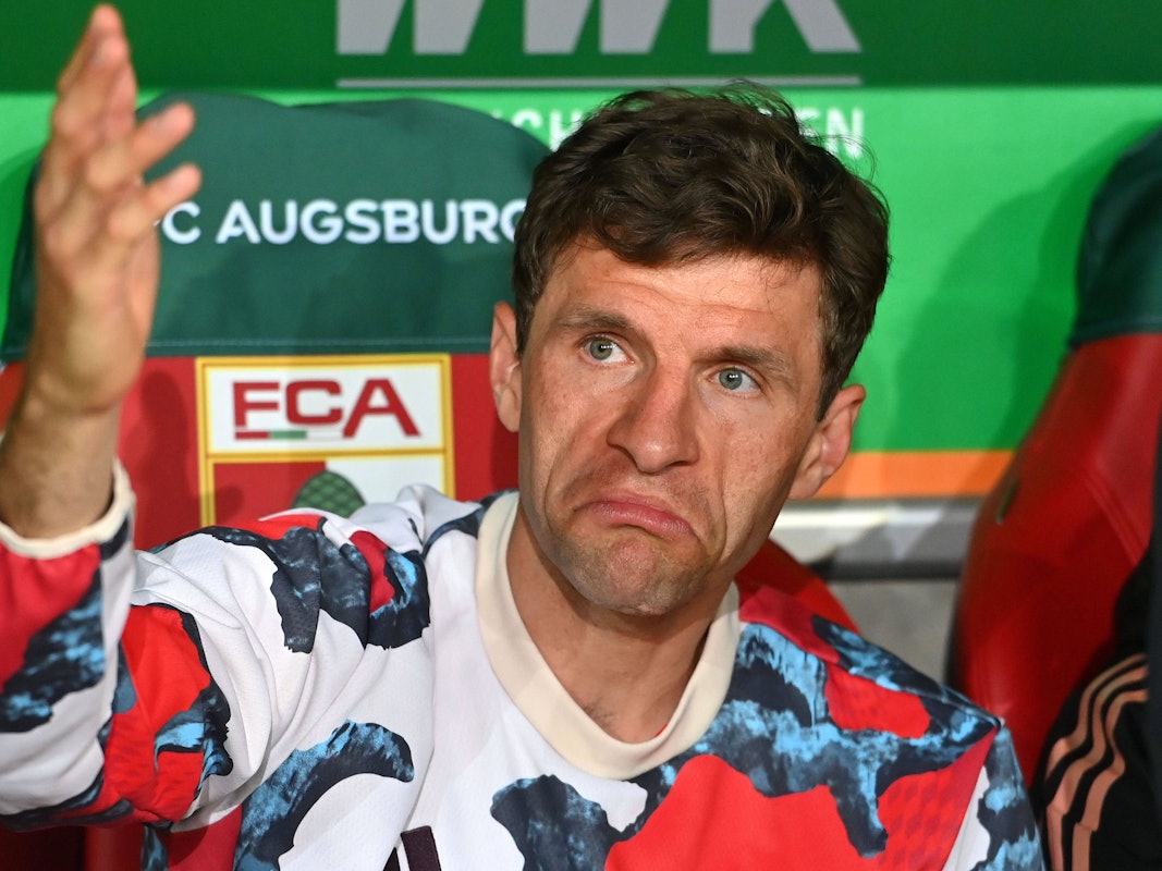 Thomas Müller sitzt auf der Ersatzbank beim FC Bayern, verzieht das Gesicht und gestikuliert.