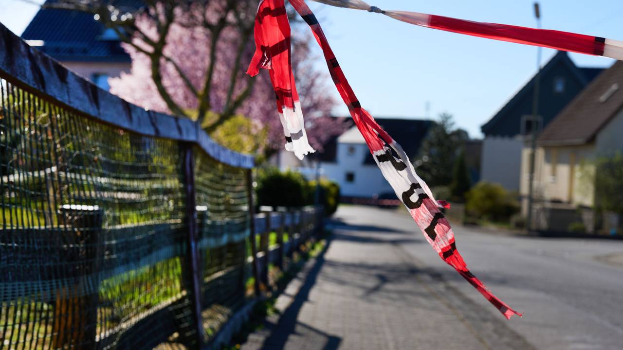 Mit Flatterband der Polizei ist eine Straße abgesperrt. Die Ermittlungen zu der Gewalttat mit drei toten Familienmitgliedern im Westerwald gehen weiter.