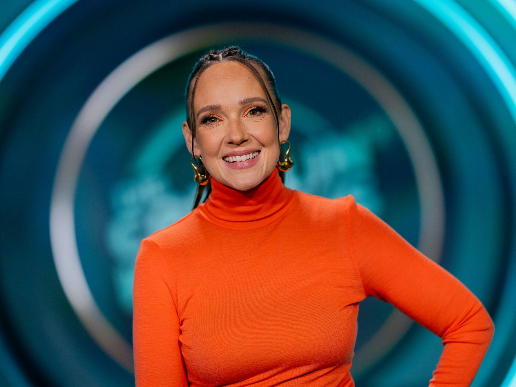 Carolin Kebekus steht im Studio und lächelt in die Kamera.