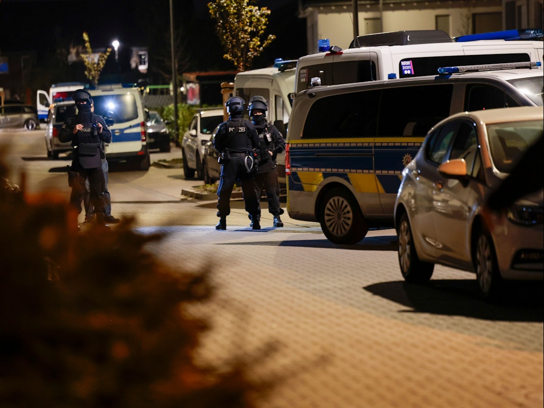 Einsatzkräfte der Polizei stehen nachts in einer Straße vor mehreren Einsatzfahrzeugen.