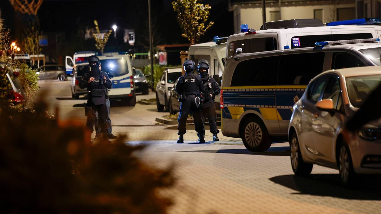 Einsatzkräfte der Polizei stehen neben geparkten Polizeifahrzeugen.