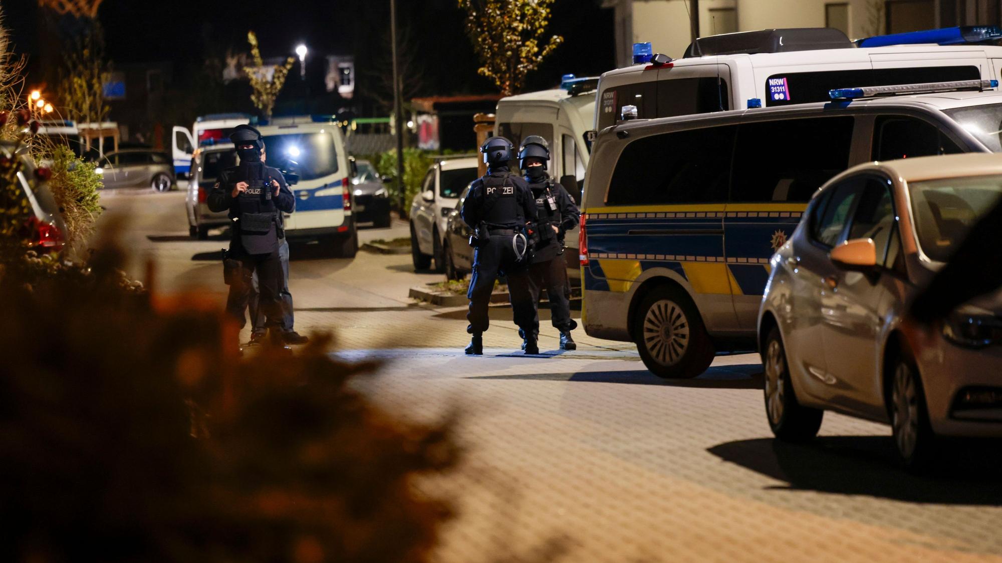 Einsatzkräfte der Polizei stehen nachts in einer Straße vor mehreren Einsatzfahrzeugen.