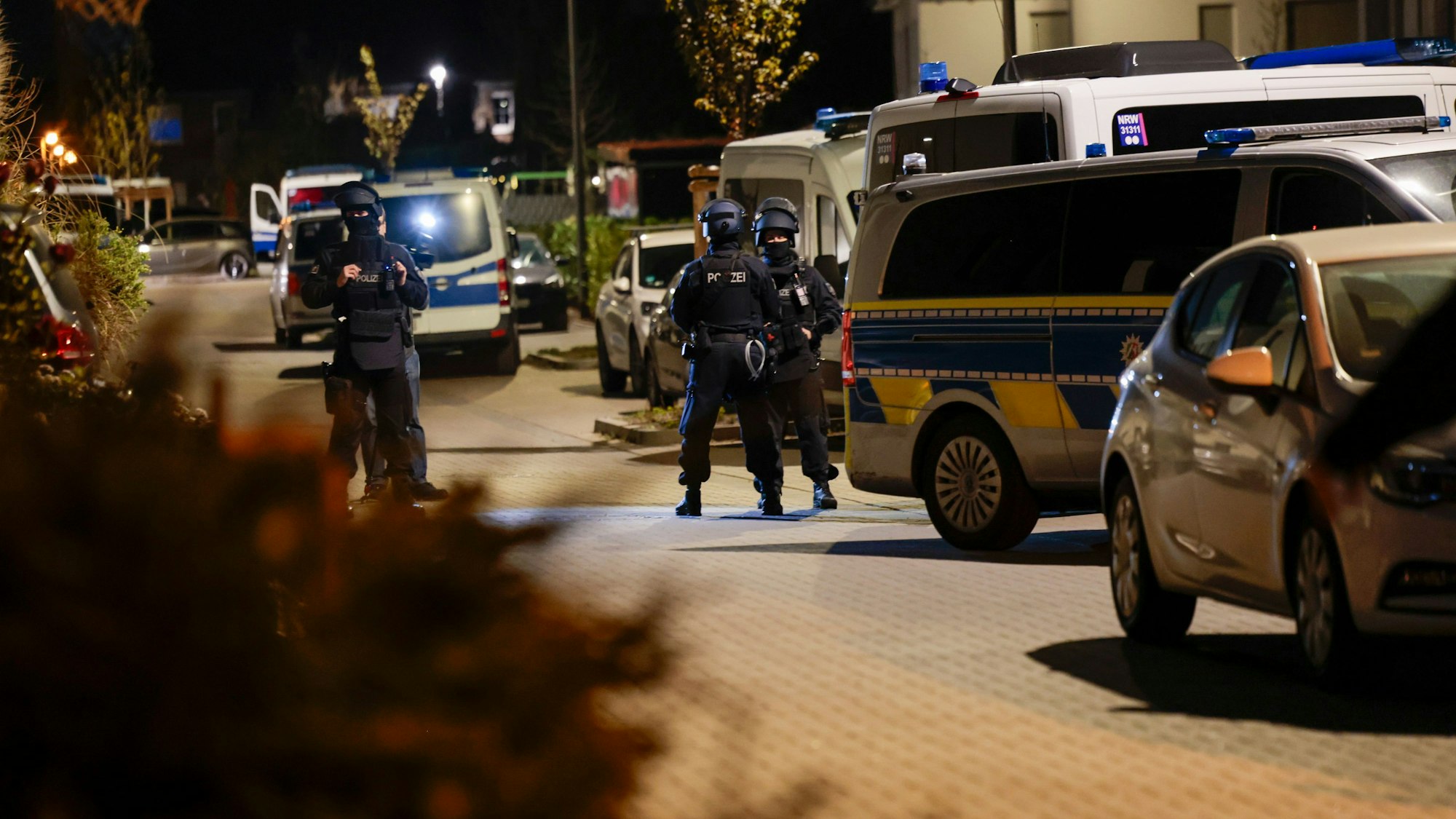 Einsatzkräfte der Polizei stehen nachts in einer Straße vor mehreren Einsatzfahrzeugen.