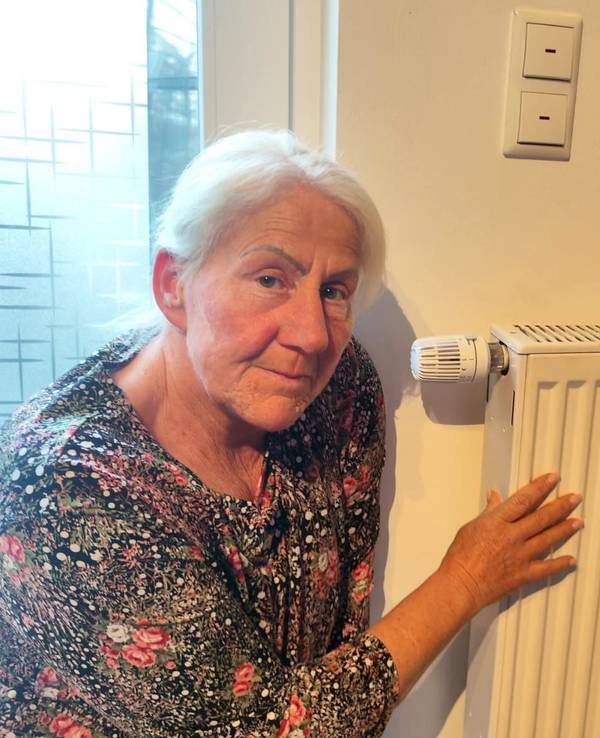 Eine Frau hockt neben einem Heizkörper in ihrer Wohnung.