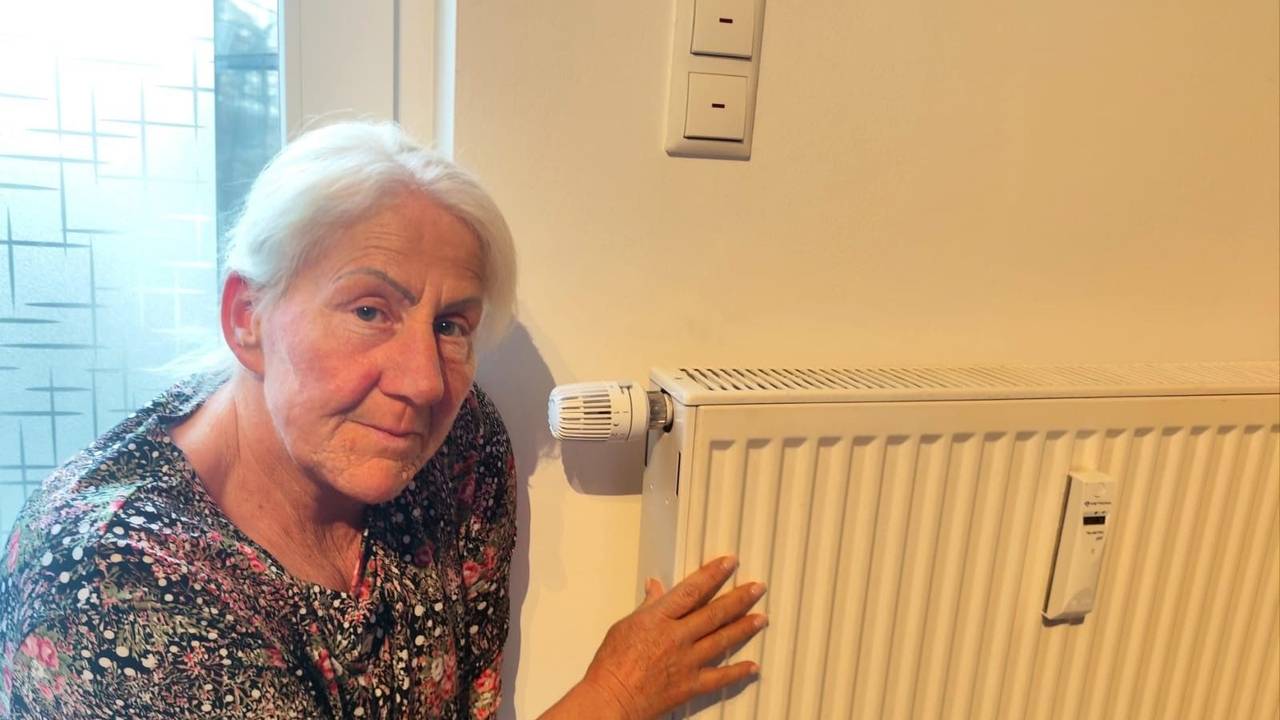 Eine Frau hockt neben einem Heizkörper in ihrer Wohnung.