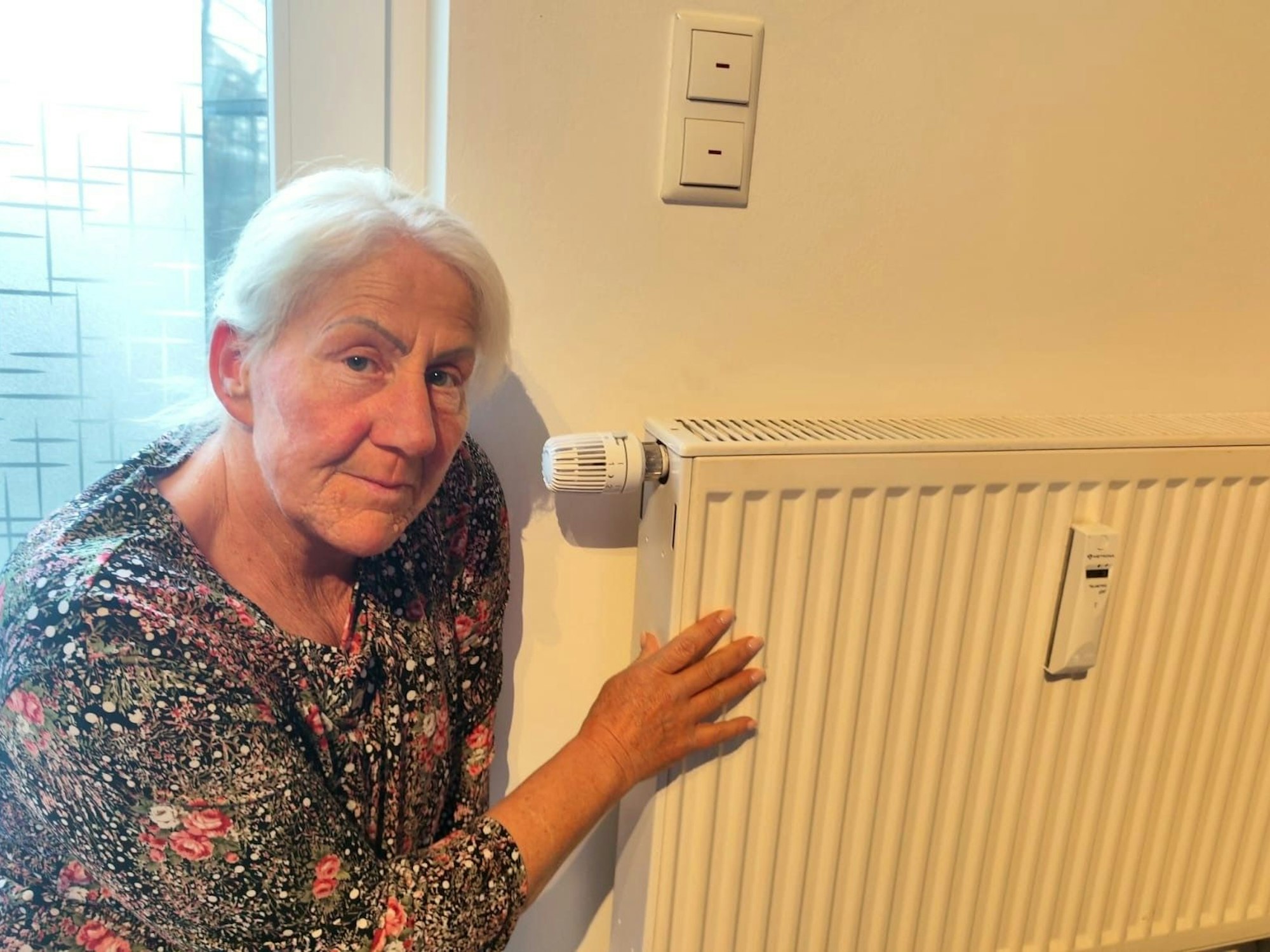 Eine Frau hockt neben einem Heizkörper in ihrer Wohnung.