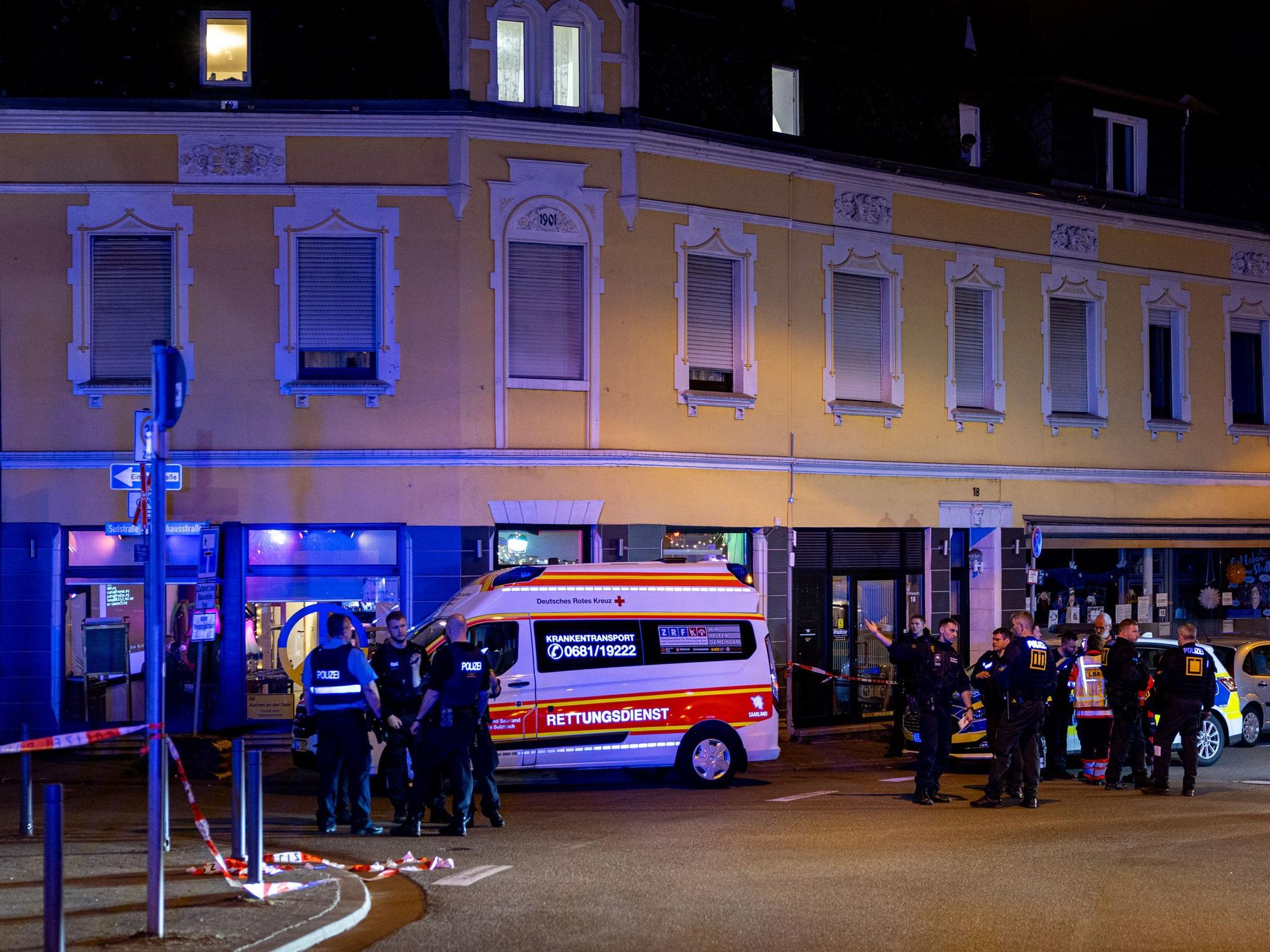 Rettungskräfte und Polizisten stehen am 11. April 2025 auf einer Straße im Saarbrücker Bezirk Dudweiler. Bei einer Auseinandersetzung mit fünf Beteiligten in Saarbrücken sind vier Menschen mit einem Messer verletzt worden.