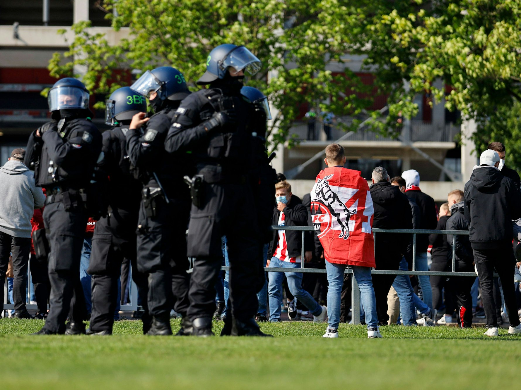 Eine Gruppe von Bundespolizisten steht auf einer Wiese und beobachtet Fans des 1. FC Köln.