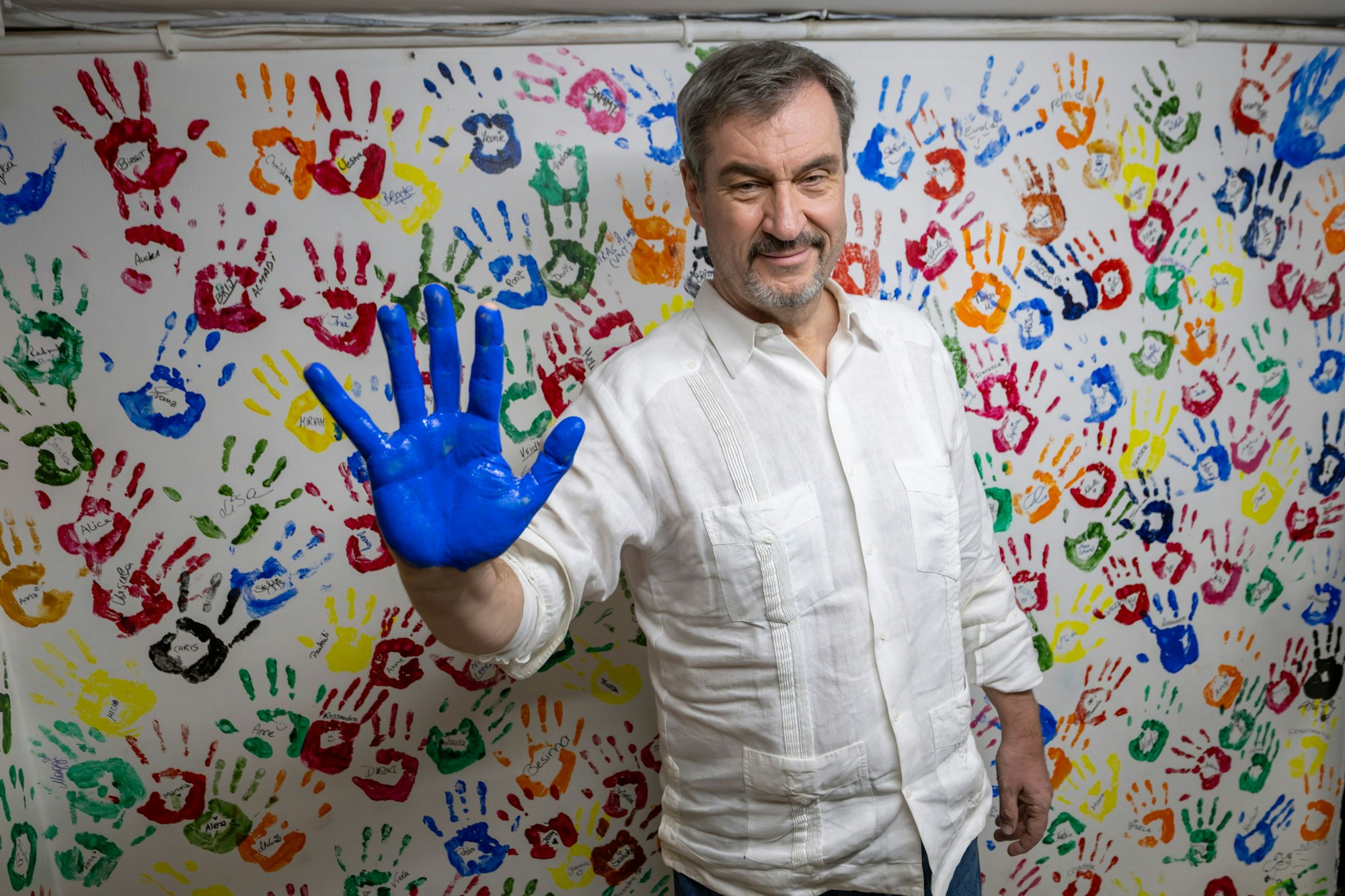 Markus Söder, (CSU) Ministerpräsident von Bayern, zeigt am 14. April 2025 in Neu-Delhi seine mit blauer Farbe bemalte Hand, damit er sich traditionsgemäß an der Wand des ‚Sunshine-Projekt‘ verewigen kann.