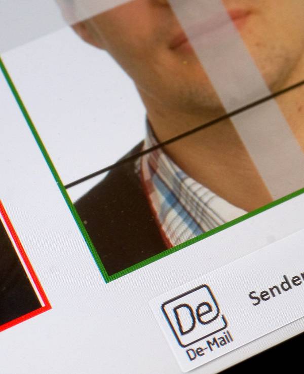 Zu sehen ist ein digital aufgenommenes biometrisches Lichtbild, das auf einem Endgerät zur elektronisch verschlüsselten Übermittlung über eine sichere Verbindung via De-Mail angezeigt wird. Ein Finger zeigt auf das Feld „Senden“ hin.