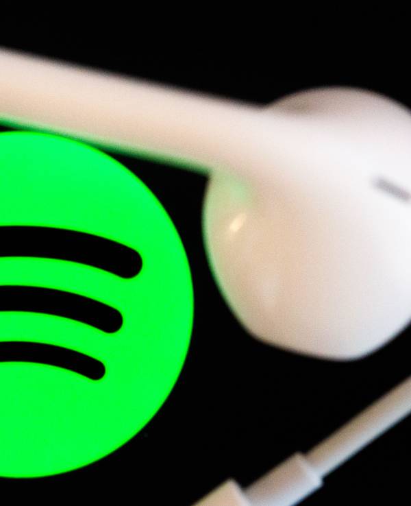 Kopfhörer liegen auf dem Bildschirm eines Smartphones, auf dem das Logo vom Musikstreaming-Dienst Spotify angezeigt wird.