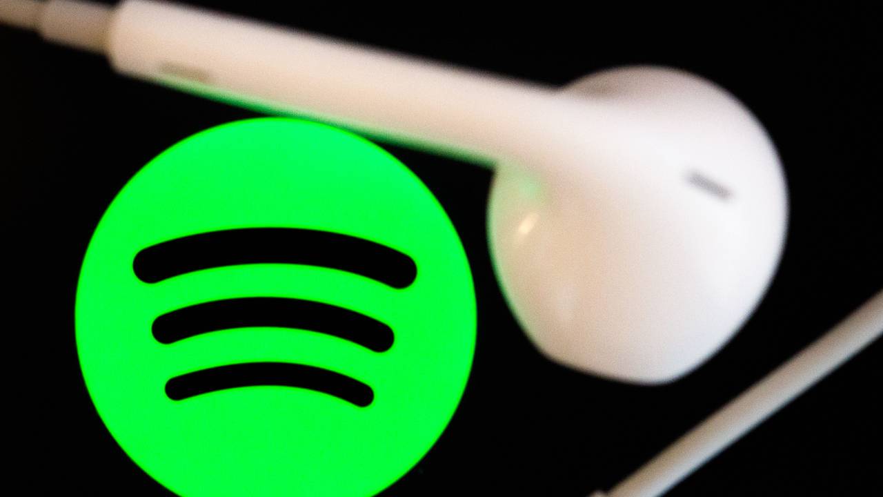 Kopfhörer liegen auf dem Bildschirm eines Smartphones, auf dem das Logo vom Musikstreaming-Dienst Spotify angezeigt wird.
