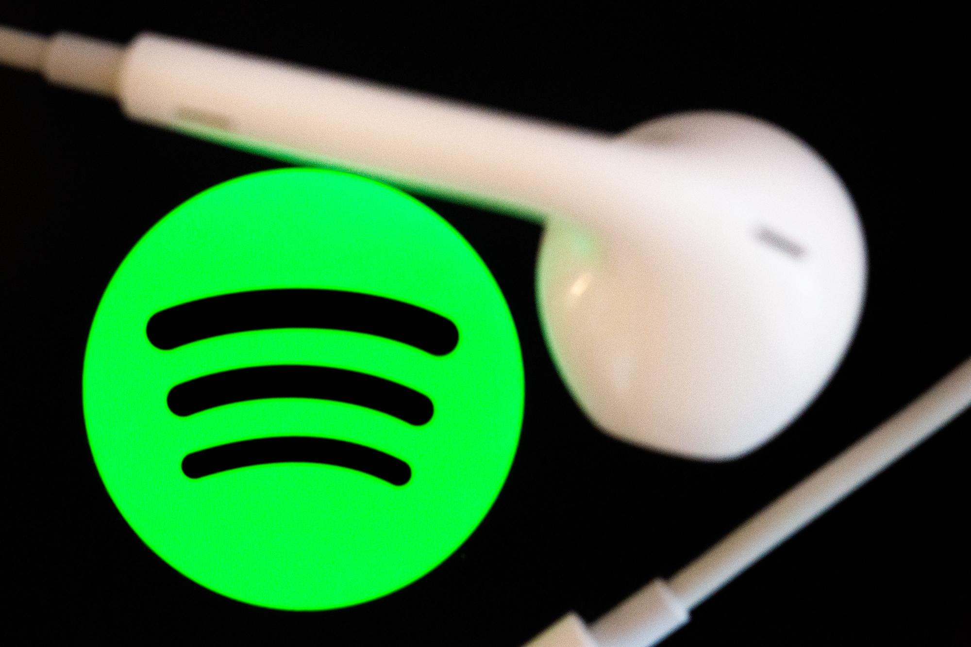 Kopfhörer liegen auf dem Bildschirm eines Smartphones, auf dem das Logo vom Musikstreaming-Dienst Spotify angezeigt wird.