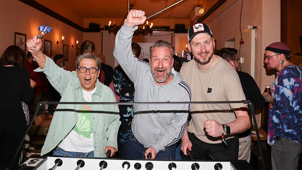 Zwei Männer und eine Frau stehen am Kickertisch und jubeln.