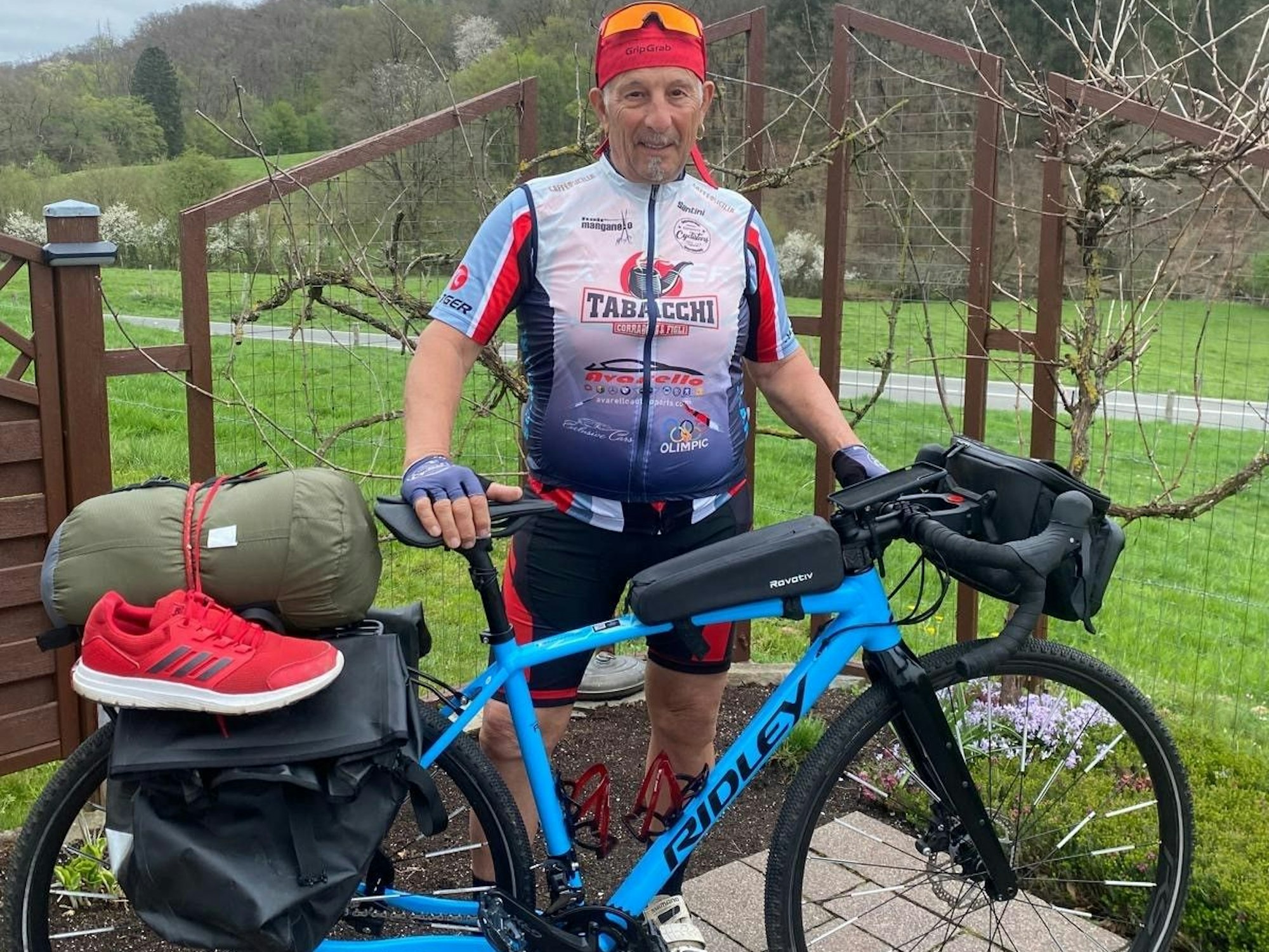 Ein Mann steht neben einem Fahrrad, das unter anderem mit einem zusammengerollten Schlafsack bepackt ist.