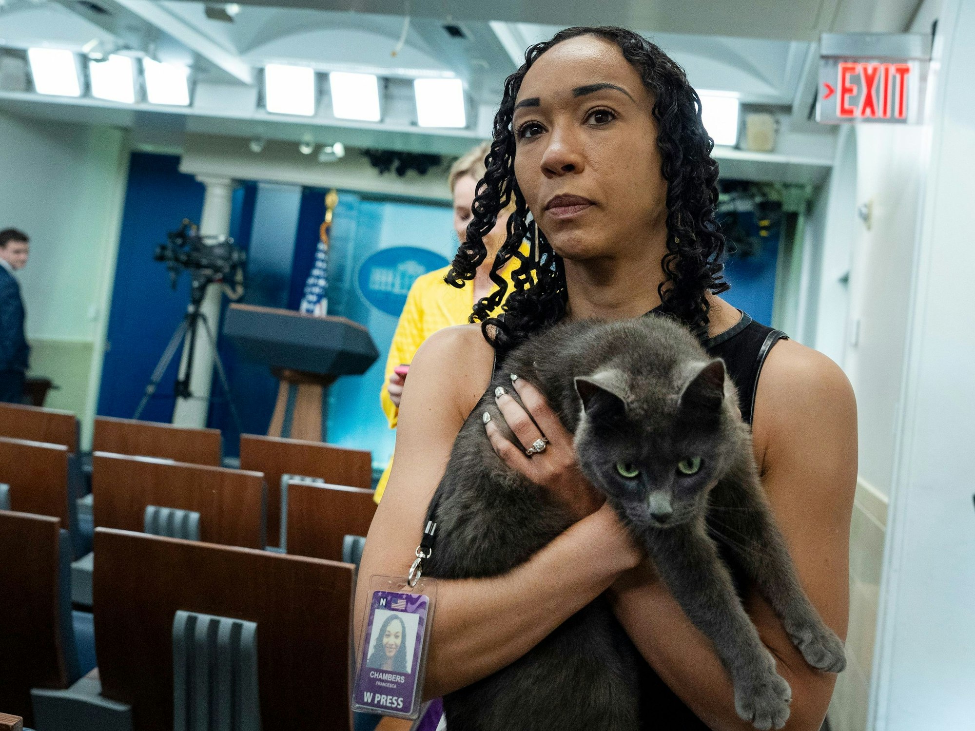 Eine Frau hält eine Katze auf dem Arm, im Hintergrund steht eine Filmkamera.